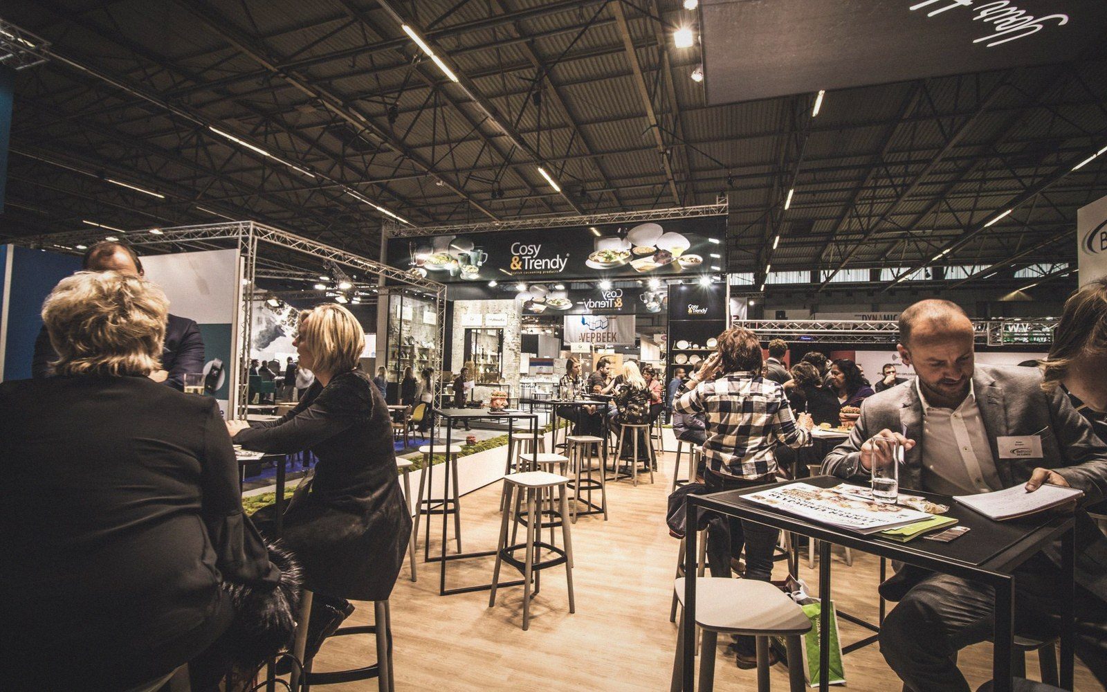 Visitors sit at high tables near the Cosy & Trendy booth inside a busy trade fair hall