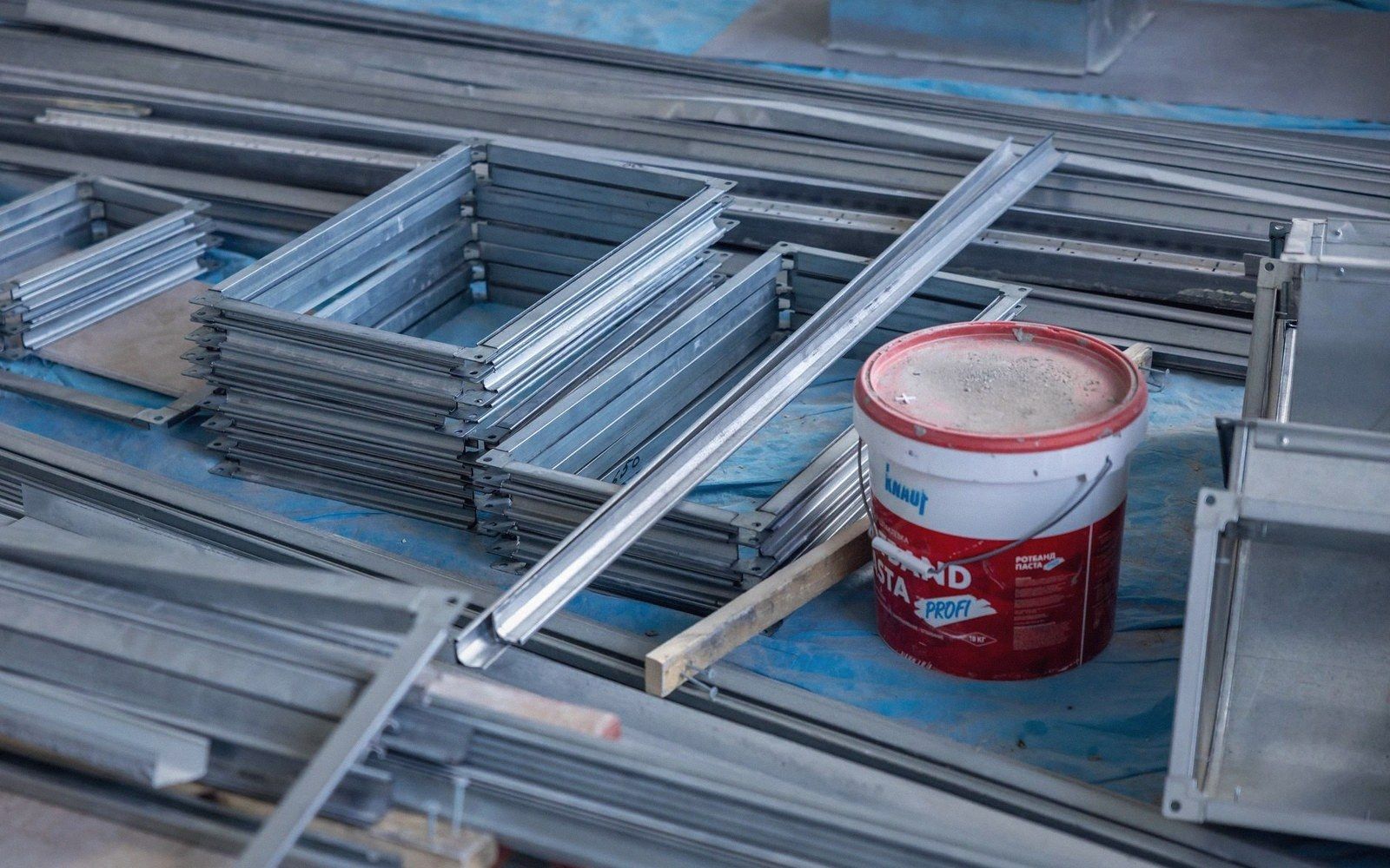 Stacked metal framing profiles and a paint bucket on a construction site tarp