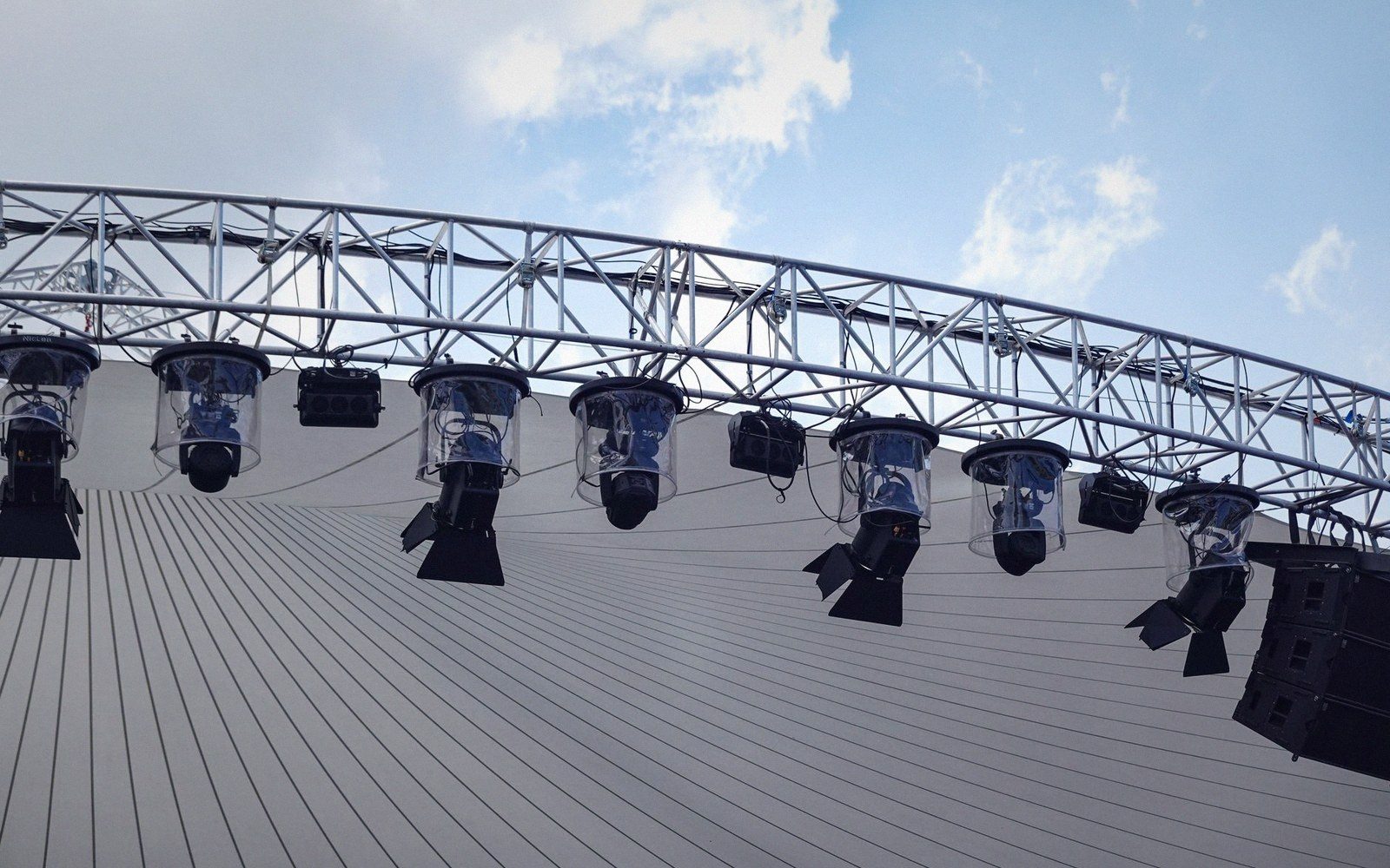 Stage lights and speakers hang from a curved truss beneath an arched canopy roof