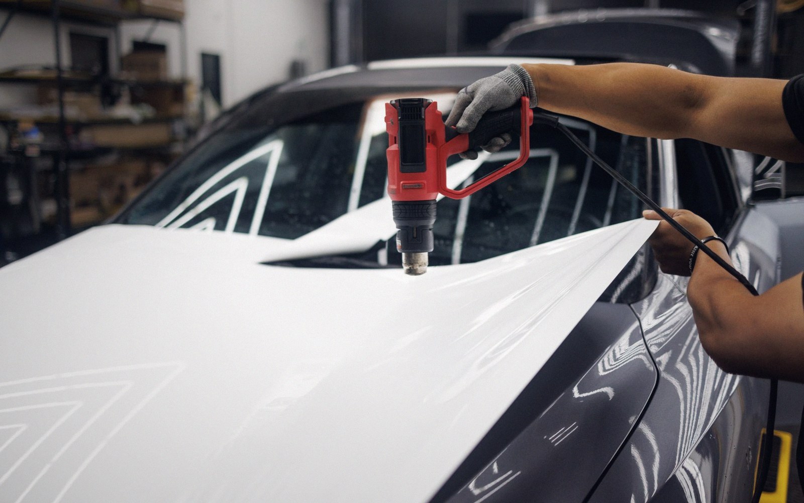 Technician uses a heat gun to apply white vinyl wrap to a car hood